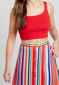 Top corto rojo con canalé y escote cuadrado, combinado con una falda de rayas multicolores que presenta rayas horizontales y detalles de botones.