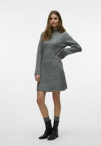 Robe tricotée grise avec une texture côtelée, encolure haute et manches longues évasées. Associée à des bottines en cuir noir et des chaussettes grises.