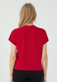Blouse rouge à manches courtes avec une texture lisse, coupe décontractée et encolure arrondie. La vue de dos montre un design épuré sans embellissements.