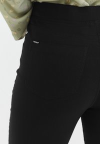 Jeans neri elasticizzati con un design aderente e una tasca sul retro. Texture liscia con dettagli di cucitura a contrasto.