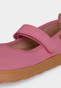 Gros plan d'une chaussure Mary Jane en tissu rose avec une bride à scratch et une semelle en caoutchouc marron clair.