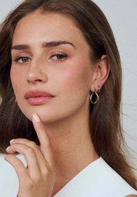 Gyllene och silverfärgade metallörhängen i en tårform med släta kurvor och en glänsande yta, båda bärs av en person med långt hår.