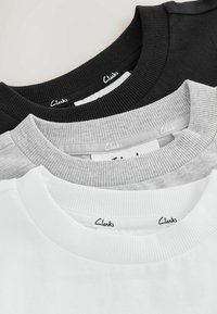 Trois T-shirts à col rond pliés en noir, gris et blanc, chacun avec un col côtelé et une étiquette Clarks visible à l'intérieur de l'encolure.