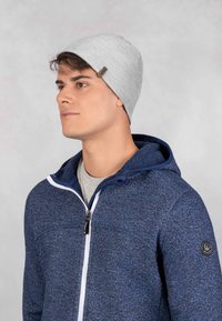 Szara dziana czapka beanie o gładkiej fakturze, noszona przez osobę w niebieskiej bluzie z zamkiem błyskawicznym z kontrastującym białym zamkiem.