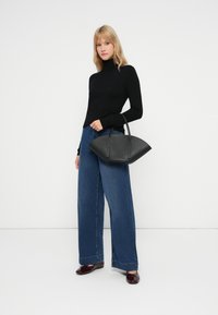 Bolsa de mão em couro preto com uma forma curvada e estruturada e duas alças, combinada com um suéter de gola alta preto e jeans azul de perna larga.