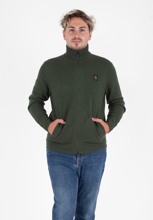 Zielona rozpinana bluza z wysokim kołnierzem, prążkowaną teksturą i dwiema przednimi kieszeniami, z małą naszywką z logo na lewej piersi.