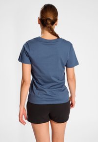 Modré bavlněné triko s krátkým rukávem, kulatým výstřihem a volným střihem, doplněné černými sportovními šortkami.