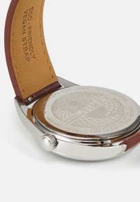 Orologio in acciaio inossidabile con cassa color argento, cinturino in pelle vegana marrone, design di un globo inciso sul retro e una corona decorativa.