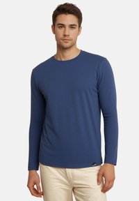 Langärmliges blaues T-Shirt aus weichem Stoff, mit rundem Halsausschnitt und einem kleinen Logohangtag am unteren Saum. Klassische Passform.