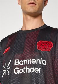 Sort og rød fodboldtrøje med et struktureret design, der har "Bayer Leverkusen" logoet og "Barmenia Gothaer" trykt i hvid.