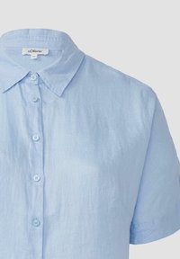 Lichtblauw kortom shirt van textuurstof. Heeft een puntige kraag en een knoopsluiting aan de voorkant, met stikseldetails langs de naden.