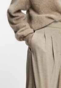 Beige knit sweater with soft, fuzzy texture and ribbed cuffs, paired with light beige pleated trousers featuring side pockets.