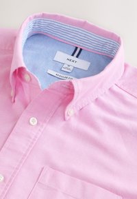 Camicia rosa chiaro con chiusura a bottoni e vestibilità regolare, caratterizzata da una fodera del colletto a righe blu e una tasca sul petto. Realizzata in cotone.