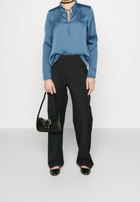Blusa di satin blu con colletto arricciato e cravatta, abbinata a pantaloni cargo neri e una piccola borsa nera a tracolla. Tessuto liscio, vestibilità comoda.