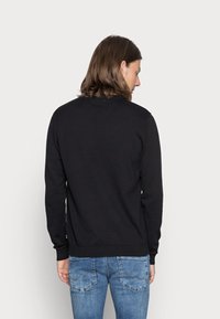 Sort strikket sweater med rund hals, ribbede ærmer og kant, båret over blå jeans. Bagsiden er ensfarvet uden synlige logoer eller mønstre.