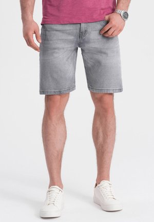 Shorts en denim gris à coupe droite, avec poches avant et ourlet uni. Portés avec des baskets blanches et un t-shirt rose ajusté.
