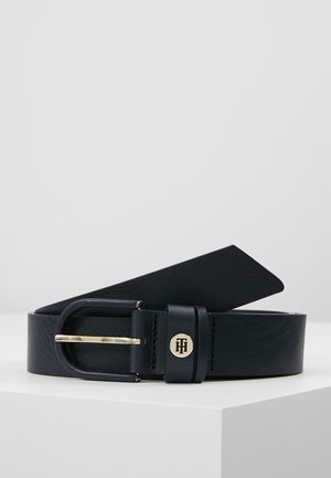 Zwarte leren riem met goudkleurige afgeronde gesp en klein goudkleurig logodetail op de riemlus, getoond op een witte ondergrond.