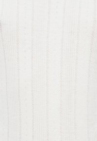 Λευκό ύφασμα πλεκτό με ριμπ υφή και κάθετες ρίγες. Διαθέτει μικρές διακοσμητικές τρύπες και μια απαλή υφή. Χωρίς ορατά μεταλλικά στοιχεία ή διακοσμήσεις.