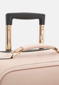 Valigia rosa chiaro con superficie texture, hardware dorato, una maniglia retrattile nera e una maniglia superiore imbottita.