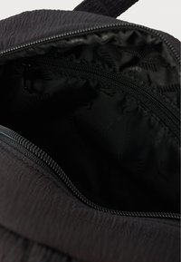 Gros plan d'une poche noire zippée à l'intérieur d'un sac, montrant la texture du tissu et la doublure intérieure avec un motif subtil.