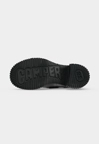 Semelle de chaussure noire avec des rainures profondes, marquage "CAMPER" en grandes lettres, et numéro de taille "38" embossé sur la zone du talon.