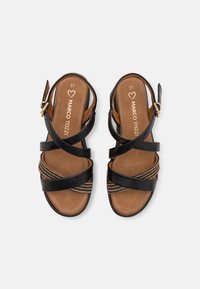 Sandales noires à lanières avec une semelle intérieure beige. Présente des accents décoratifs tressés et une fermeture à boucle sur le côté. Taille 37. Texture en cuir lisse.