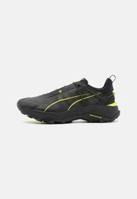 Scarpe da ginnastica nere con tessuto texturizzato, dettagli gialli e suola robusta. Presentano un sistema di allacciatura sicuro e un tallone rinforzato.
