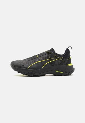 Scarpe da ginnastica nere con tessuto texturizzato, dettagli gialli e suola robusta. Presentano un sistema di allacciatura sicuro e un tallone rinforzato.