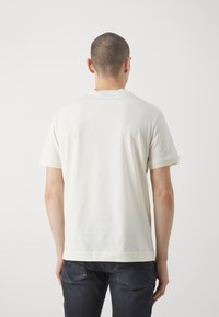 Koszulka z krótkim rękawem i okrągłym dekoltem wykonana z kremowej bawełny. Posiada prążkowane wykończenia na rękawach i na dole, a całość charakteryzuje się gładką fakturą.