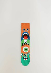 Chaussettes colorées avec un design de trois monstres dans des teintes orange, verte et bleue, avec de grands yeux et des dents. Fabriquées en tissu doux.
