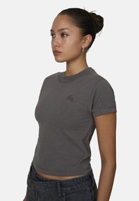 Grijze, kortemouwen crop top gemaakt van textuurstof, met een ronde hals en een geborduurd logo op de borst, gecombineerd met blauwe denim jeans.
