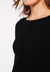Pull noir côtelé avec col rond et silhouette ajustée, présentant une texture lisse et des détails subtils le long des coutures.