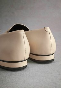 Chaussures en cuir beige avec une texture lisse, des talons arrondis, des coutures discrètes et une semelle noire basse. Design simple et moderne.