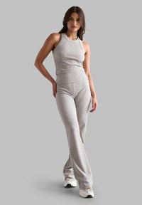 Top a maniche corte grigio a costine e pantaloni a flared abbinati, entrambi attillati, con una texture liscia. La modella indossa sneakers bianche, sullo sfondo grigio.