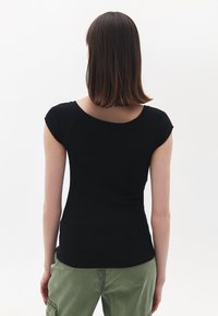 T-shirt nera aderente con maniche corte e scollatura rotonda, realizzata in tessuto a coste, indossata con pantaloni cargo verdi, mostrando una vista posteriore semplice.