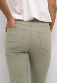 Jeans elásticos verdes con un diseño ajustado. Los detalles notables incluyen dos bolsillos traseros y una textura suave. El dobladillo cae por encima del tobillo.