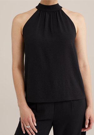 Vrouw draagt een mouwloze zwarte haltertop gecombineerd met zwarte broek, met een minimalistisch en elegant outfitdetail.