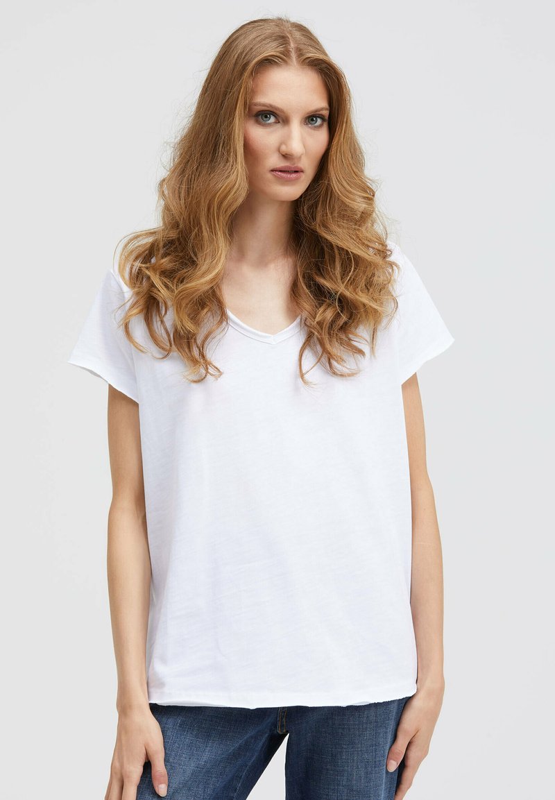 White short-sleeve V-neck t-shirt made of soft cotton, featuring a relaxed fit and simple design. Paired with blue denim jeans.