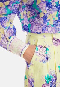 Blumenbluse in lila und gelben Farbtönen mit puffärmel. Passende, hoch taillierte Hose in hellgelb mit lila Blumendrucken.