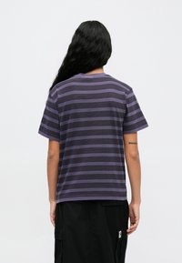 Vijolična majica s kratkimi rokavi, okroglim izrezom in sproščenim krojem. Ima horizontalne črne črte in mehak material.