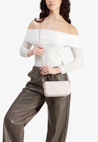 Borsa a tracolla rosa chiaro realizzata in pelle liscia con una tracolla in catena dorata. Presenta una forma rettangolare e un logo in rilievo sottile.