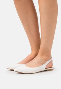 Weiße flache Schuhe mit einer spitzen Zehenpartie, aus glattem Material, mit Slingback-Design und einer niedrigen, flachen Sohle.