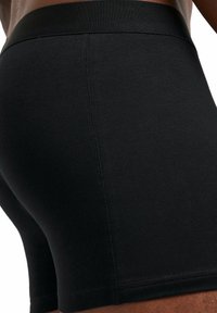 Boxer shorts noirs avec une texture lisse, une taille élastique et un design ajusté, présentant une construction sans couture et une couleur unie.