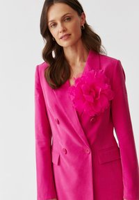 Fuchsiový blazer s dvouvrstvým designem, texturovanou látkou a velkým dekoračním květinovým akcentem na levé hrudi.