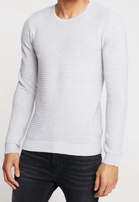 Pull gris clair côtelé à manches longues, col rond et texture subtile, associé à un jean foncé.