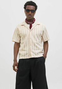 Chemise à col à manches courtes avec des rayures verticales beige clair et crème. Le matériau semble texturé. Pantalons amples noirs avec poches.