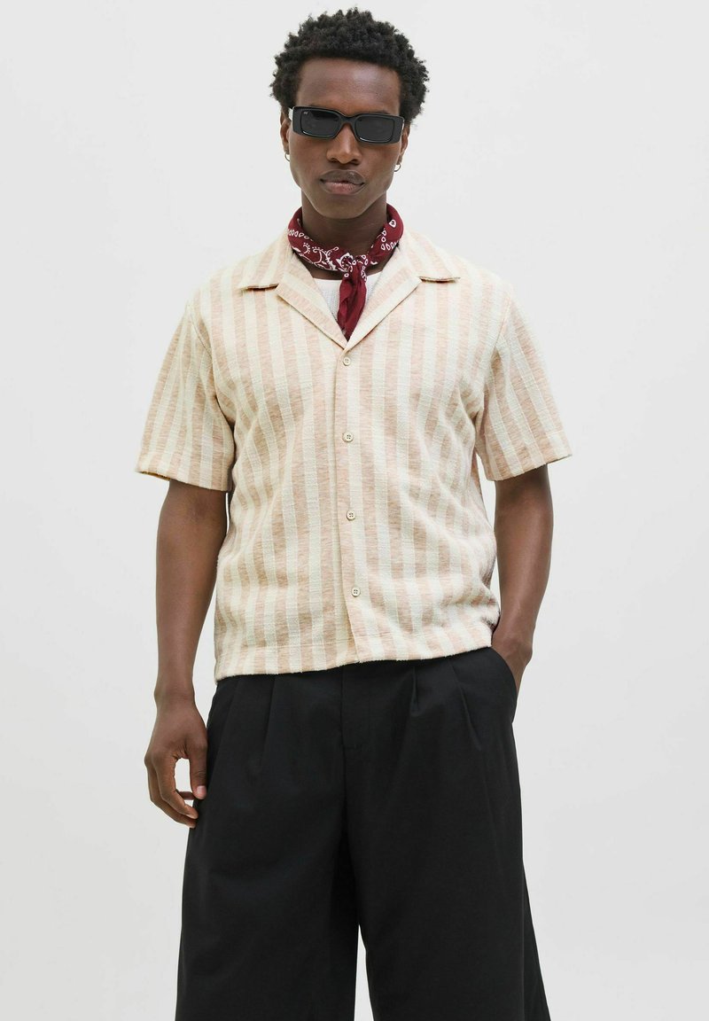 Chemise à col à manches courtes avec des rayures verticales beige clair et crème. Le matériau semble texturé. Pantalons amples noirs avec poches.