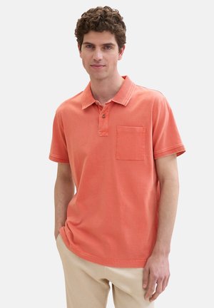 Korallfarbenes Poloshirt mit Kragen, einer Brusttasche und kurzen Ärmeln. Hergestellt aus weichem Baumwollstoff mit Steppdetails am Kragen.