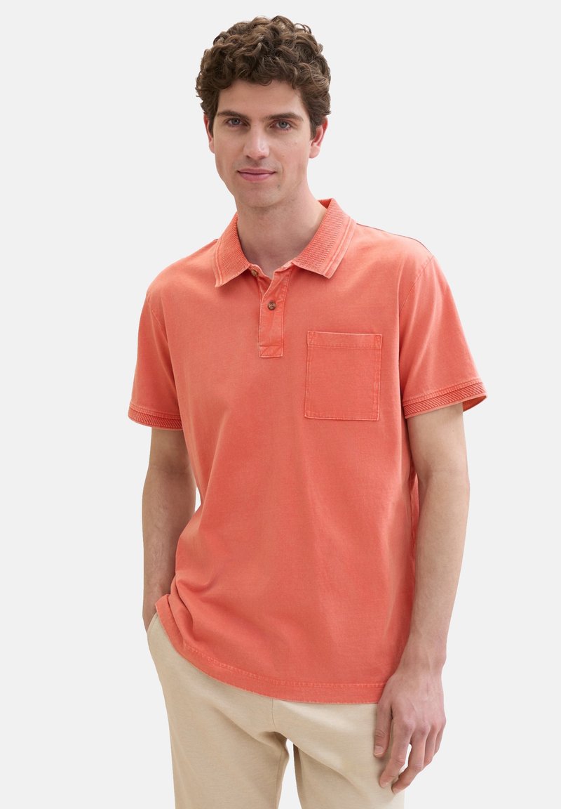 Korallfärgad polo-shirt med krage, bröstficka och korta ärmar. Tillverkad av mjuk bomullstyg med sömdetaljer på kragen.