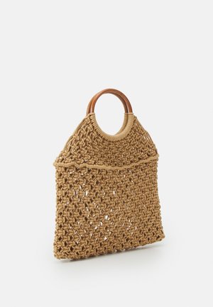 Sac fourre-tout marron en tissu tissé avec des poignées circulaires en bois et un motif en maille ouverte, posé debout sur une surface blanche.